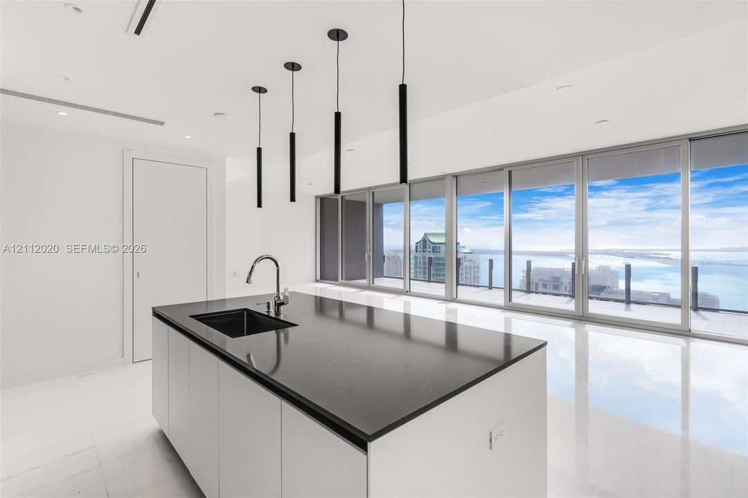 Center island featuring a dark stone countertop, integrated sink, and matte black faucet, complemented by minimalist pendant lighting and floor-to-ceiling glass sliding doors