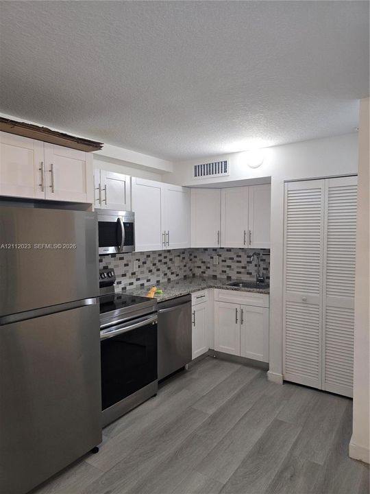 Kitchen featuring shaker-style cabinetry, stainless steel appliances, multi-toned stone-finish backsplash, speckled stone-finish countertops, and wood-finish flooring