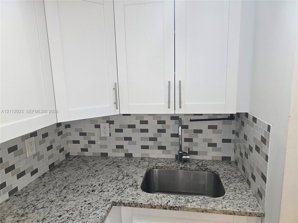 Shaker-style white cabinetry, speckled stone countertop, stainless steel undermount sink, gooseneck faucet, and multi-toned rectangular tile backsplash
