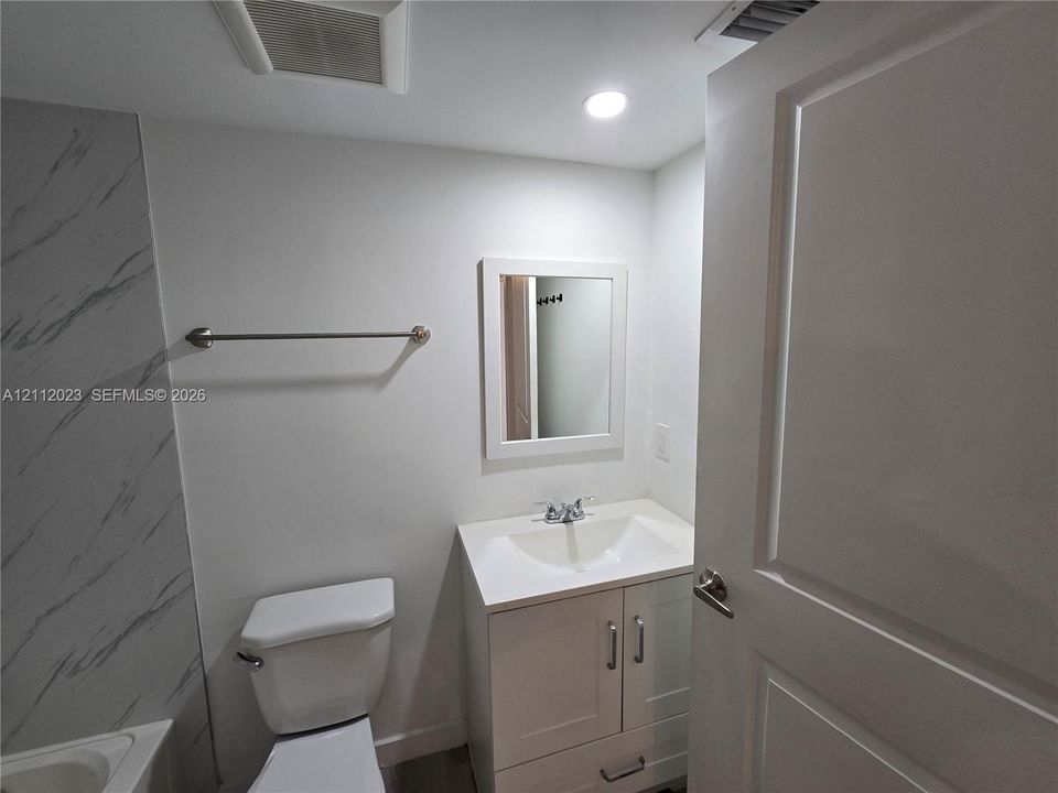 White vanity with integrated basin, polished metal faucet, wall-mounted mirror, and stone-finish wall tile surround