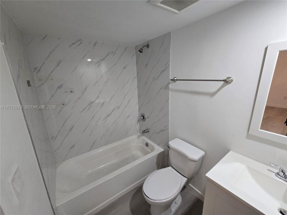 Bathroom featuring a shower and tub combination with wall-surround tile, vanity with a white countertop, wood-finish flooring, and a wall-mounted towel bar