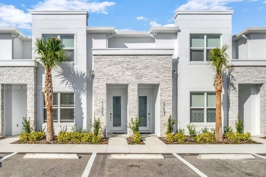 Modern townhouse exterior featuring a smooth stucco finish, textured stone facade accents, recessed entryways, and dedicated parking spaces