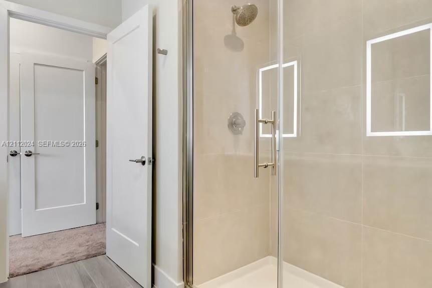 Glass-enclosed shower with metallic fixtures, recessed wall niches, neutral-toned wall tile, and white Shaker-style doors
