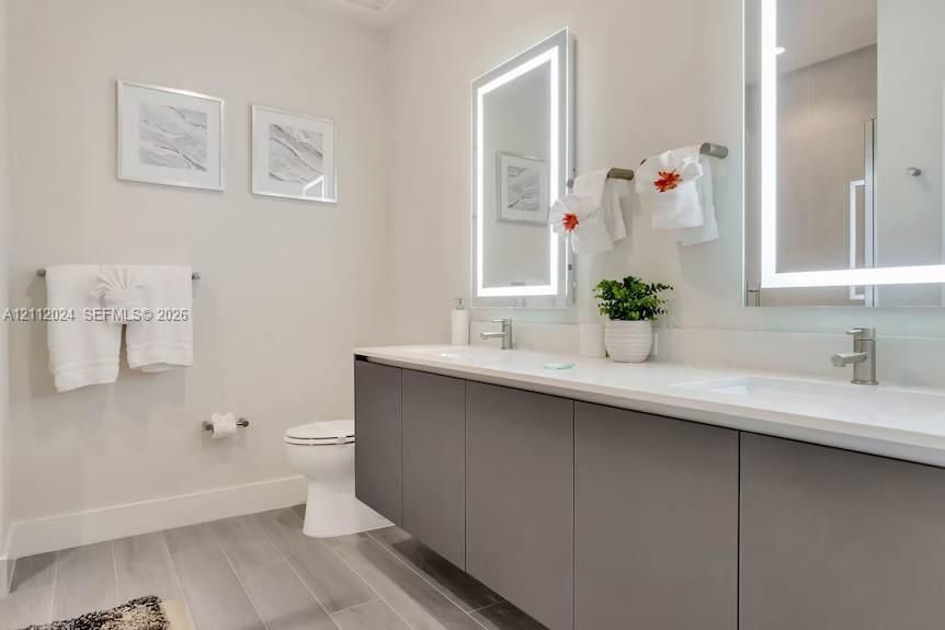 Floating double vanity with a light-toned countertop, dual rectangular undermount sinks, illuminated vanity mirrors, and gray wood-finish floor tiling