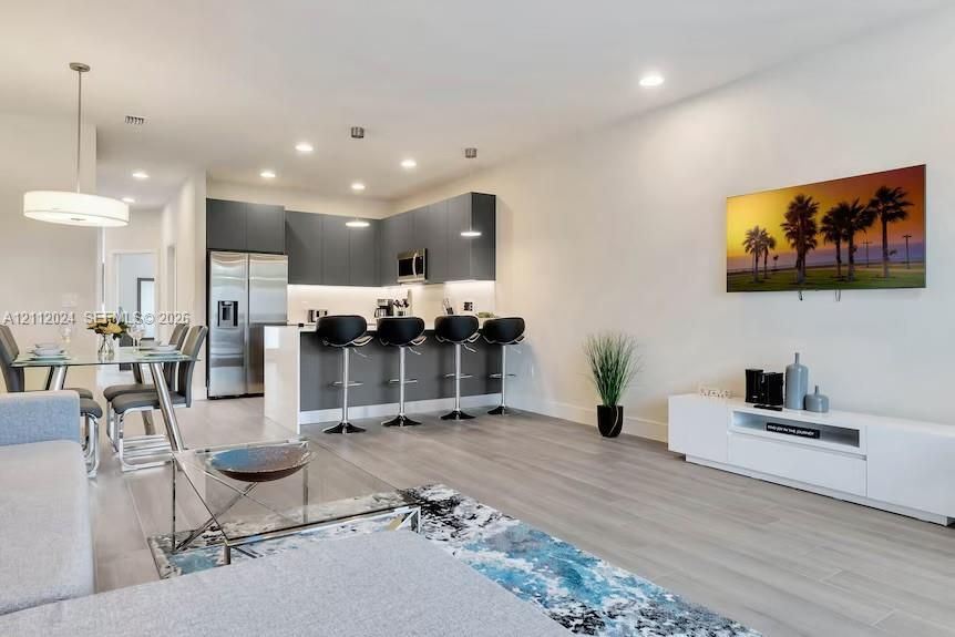 Open-concept kitchen featuring flat-panel cabinetry, quartz countertops, stainless steel appliances, recessed lighting, and wood-finish flooring