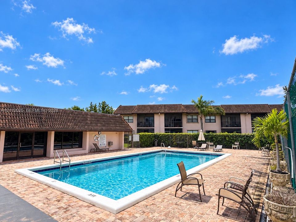 In-ground swimming pool featuring a brick-paver deck, metal pool ladder, and privacy hedging