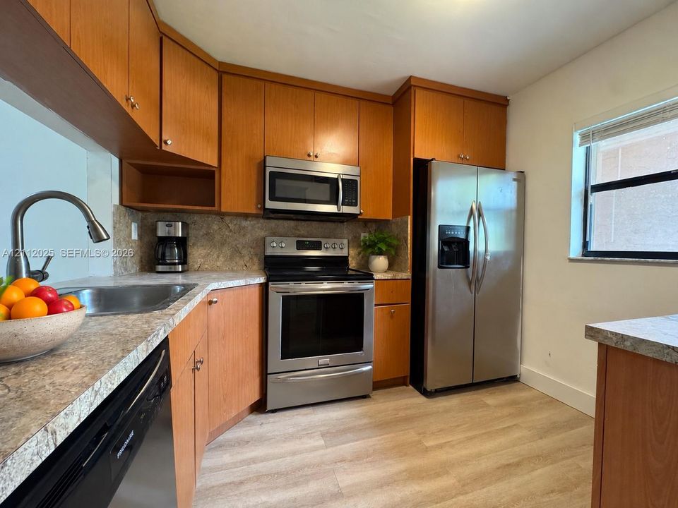 Kitchen featuring wood cabinetry, stainless steel appliances, laminate countertops, a stainless steel sink with a pull-down faucet, and wood-finish flooring