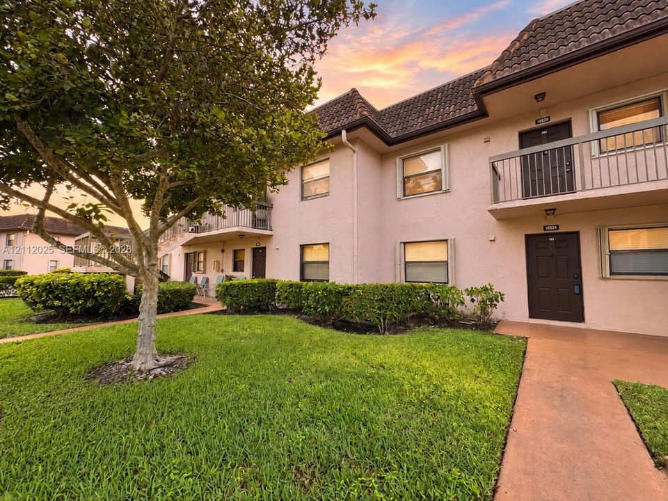 Stucco exterior featuring a tile roof, private balcony, and manicured landscaping