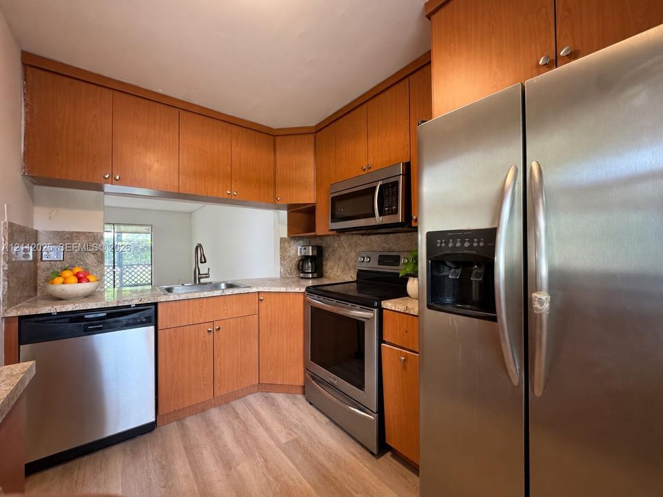 Kitchen featuring medium-tone wood cabinetry, stone-finish countertops, stainless steel appliances, and wood-finish flooring