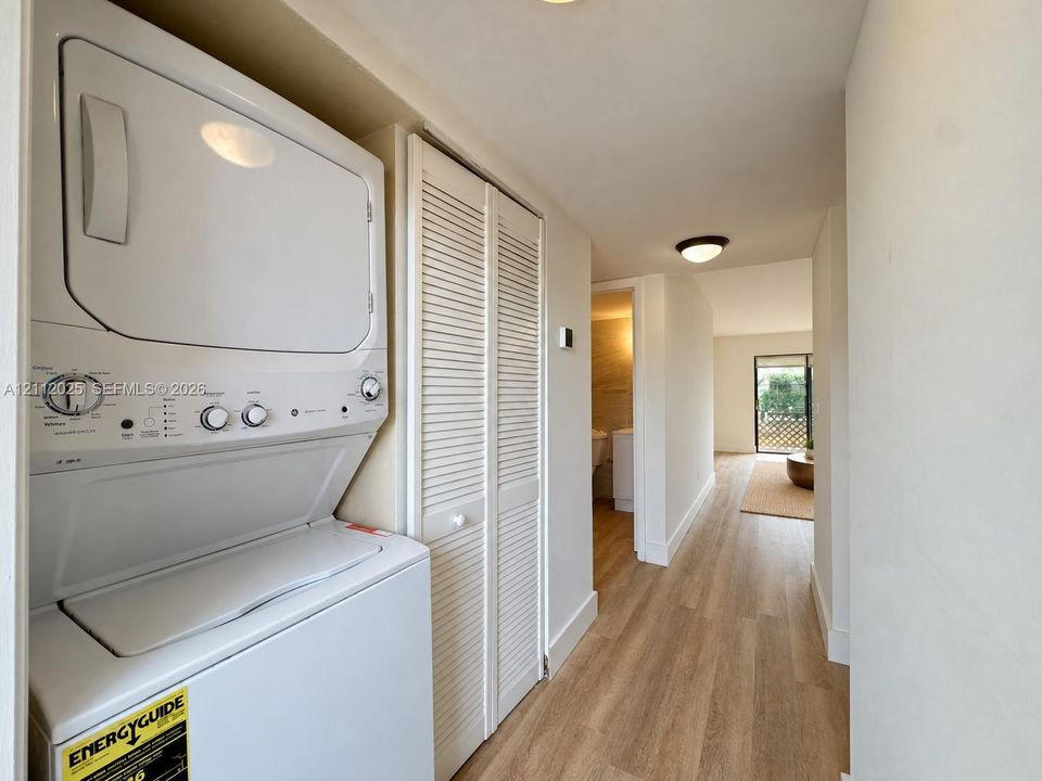 Laundry area featuring a stacked washer and dryer unit, louvered closet doors, and wood-finish flooring