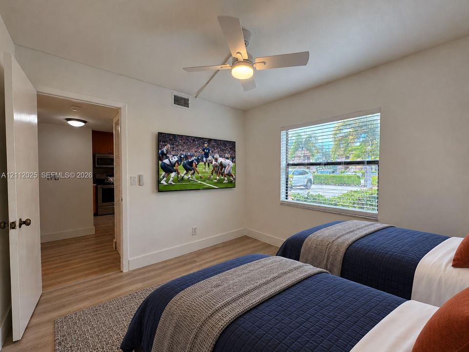 Neutral interior featuring light wood-finish flooring, a wall-mounted ceiling fan with integrated lighting, and a large horizontal window with fitted blinds