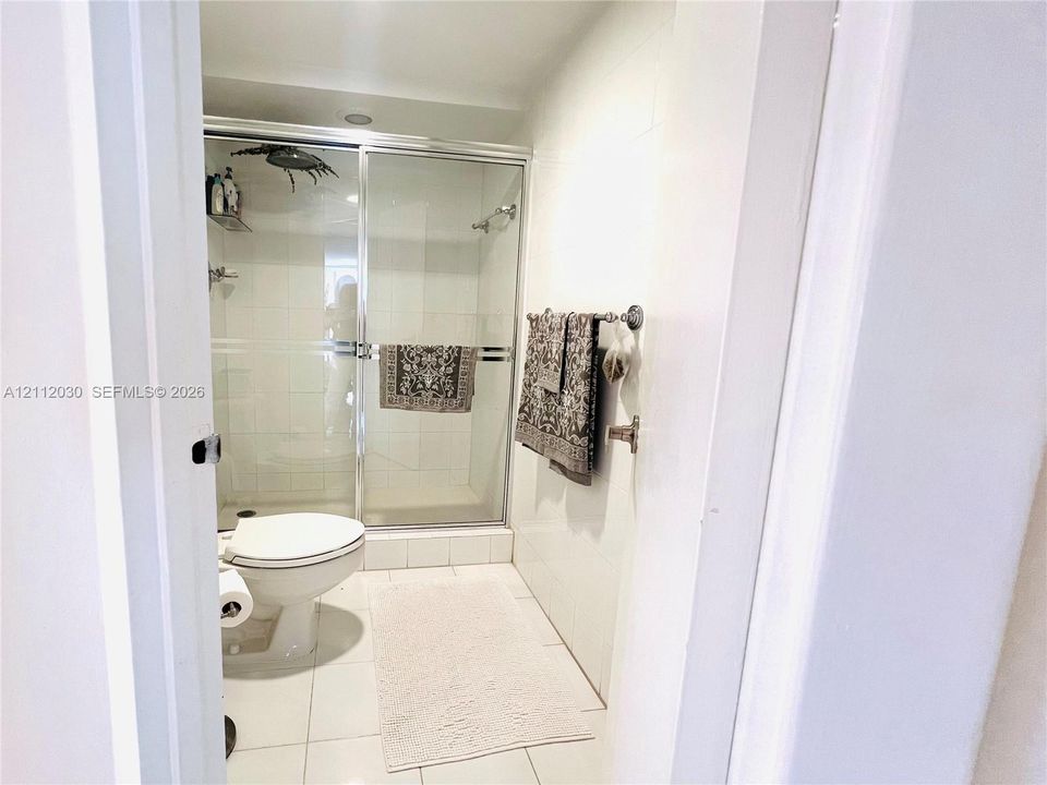 Bathroom featuring a shower stall with a glass sliding door, white tile wall surfacing, ceramic tile flooring, and a chrome-finish shower fixture