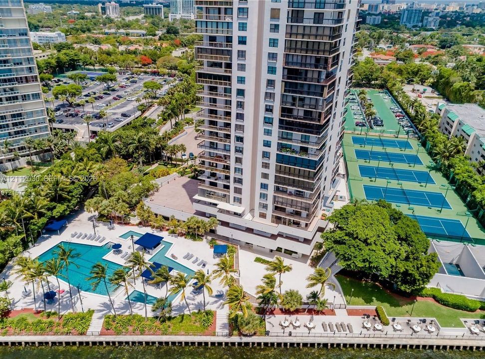 High-rise condominium tower featuring a resort-style swimming pool, multiple tennis courts, private marina access, and landscaped grounds