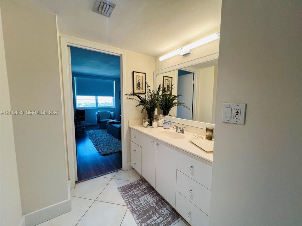 Vanity featuring a solid-surface countertop, integrated oval sink, chrome dual-handle faucet, white cabinetry with crystal-style hardware, and a full-width mirror with linear lighting