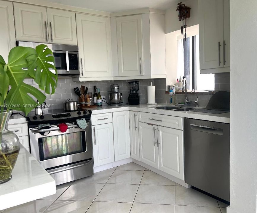 Kitchen featuring white shaker-style cabinetry, stainless steel appliances, subway tile backsplash, solid-surface countertops, and diagonal-set tile flooring