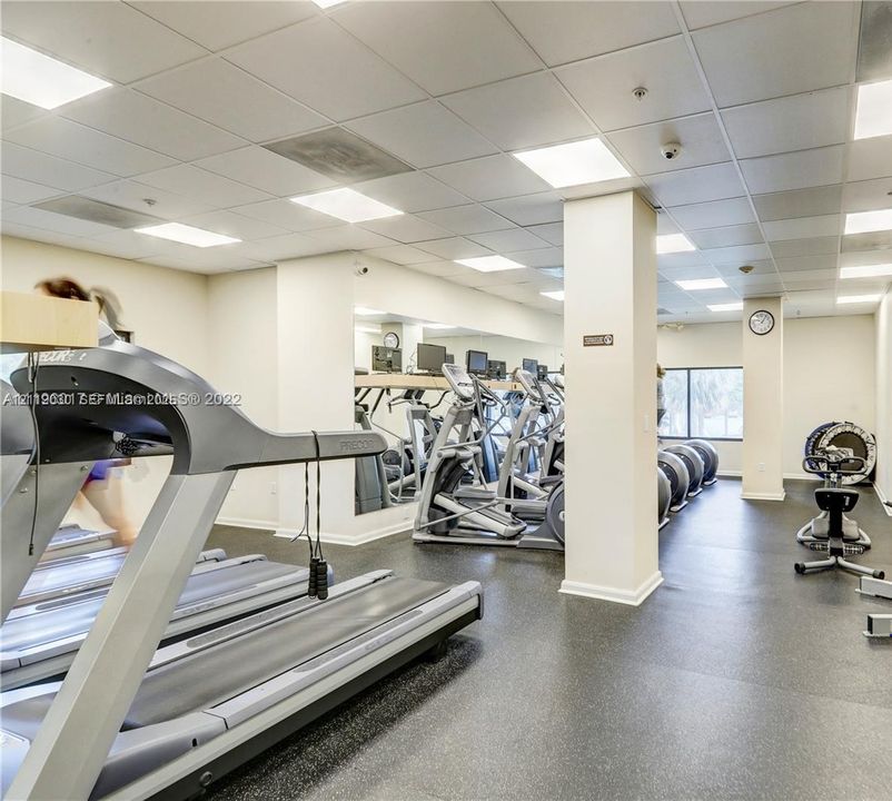 Fitness center featuring grid ceiling lighting, wall-to-wall mirrors, and resilient rubberized flooring