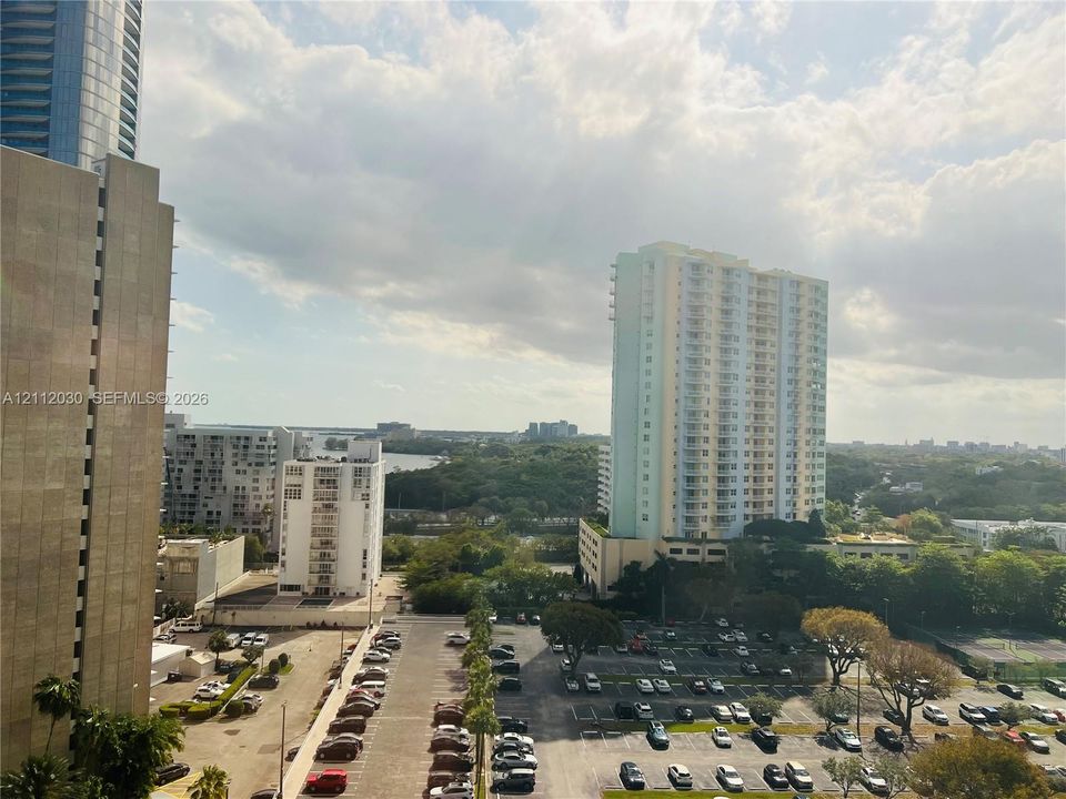 High-rise exterior elevation featuring a dense urban landscape, multi-story residential structures, paved parking areas, and mature trees