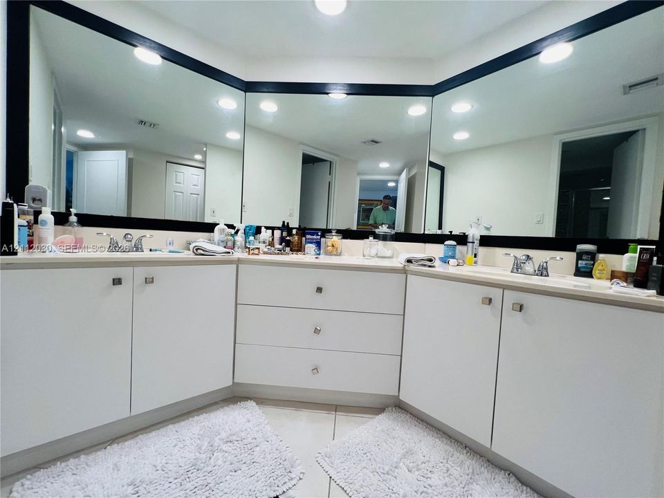 L-shaped dual vanity featuring white cabinetry, polished metal hardware, expansive wall-to-wall mirrors, and dual chrome faucets