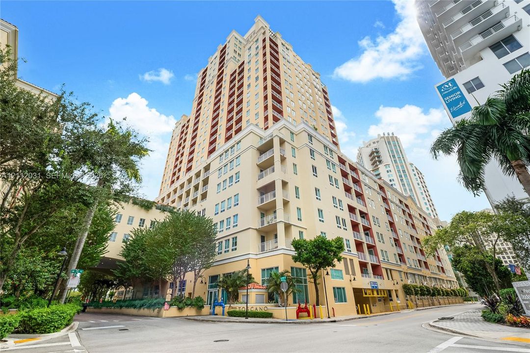 High-rise residential building featuring a multi-story facade, recessed private balconies, ground-level covered entryway, and exterior stucco finish