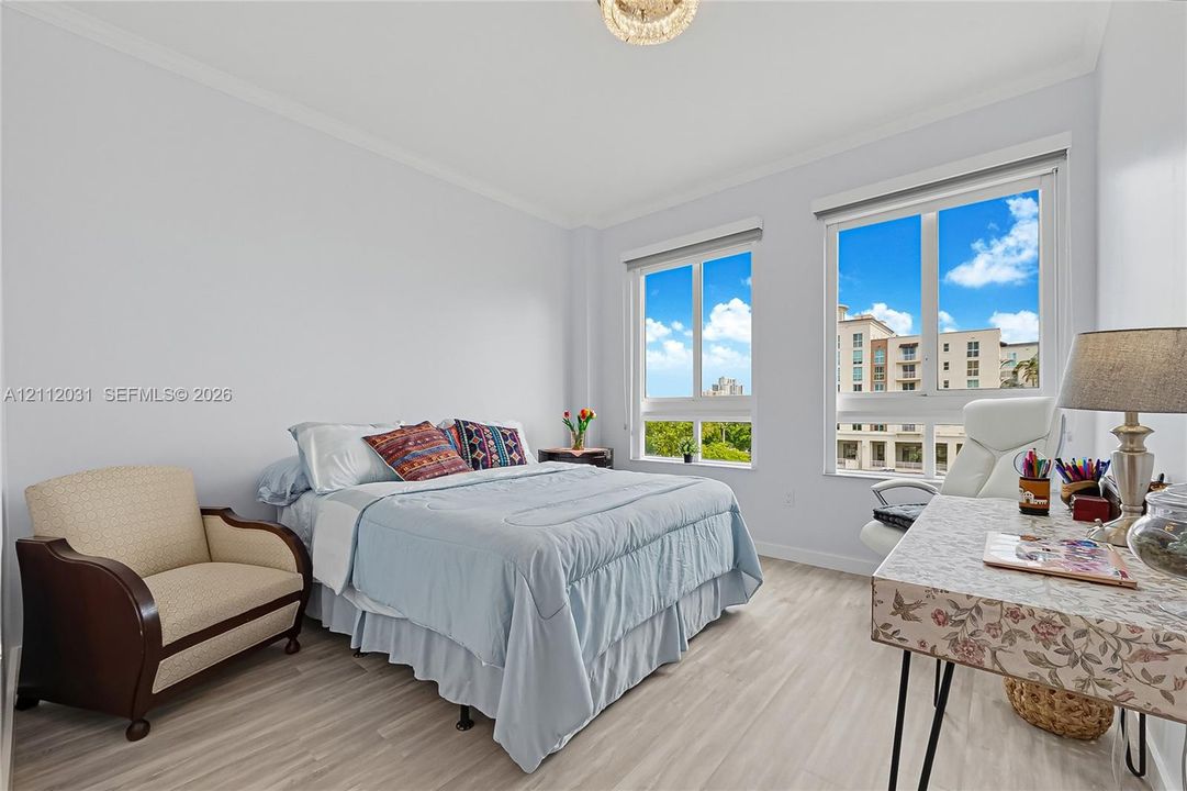Room featuring light-toned wood-finish flooring, dual windows with exterior urban scenery, crisp white walls, crown molding, and a decorative ceiling-mounted fixture