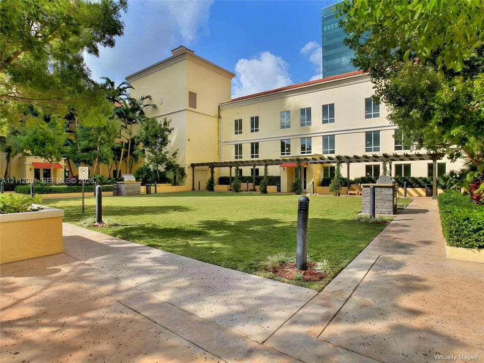 Exterior courtyard featuring a manicured lawn, pergola-covered walkways, stone-finished grill stations, and established landscape borders, BBQ area
