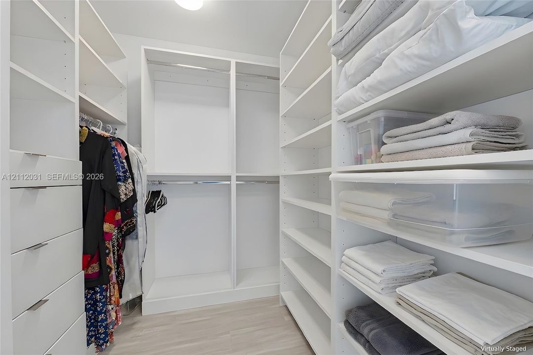 Walk-in closet featuring white built-in shelving, integrated dresser drawers with metal pulls, and dual-level hanging rods