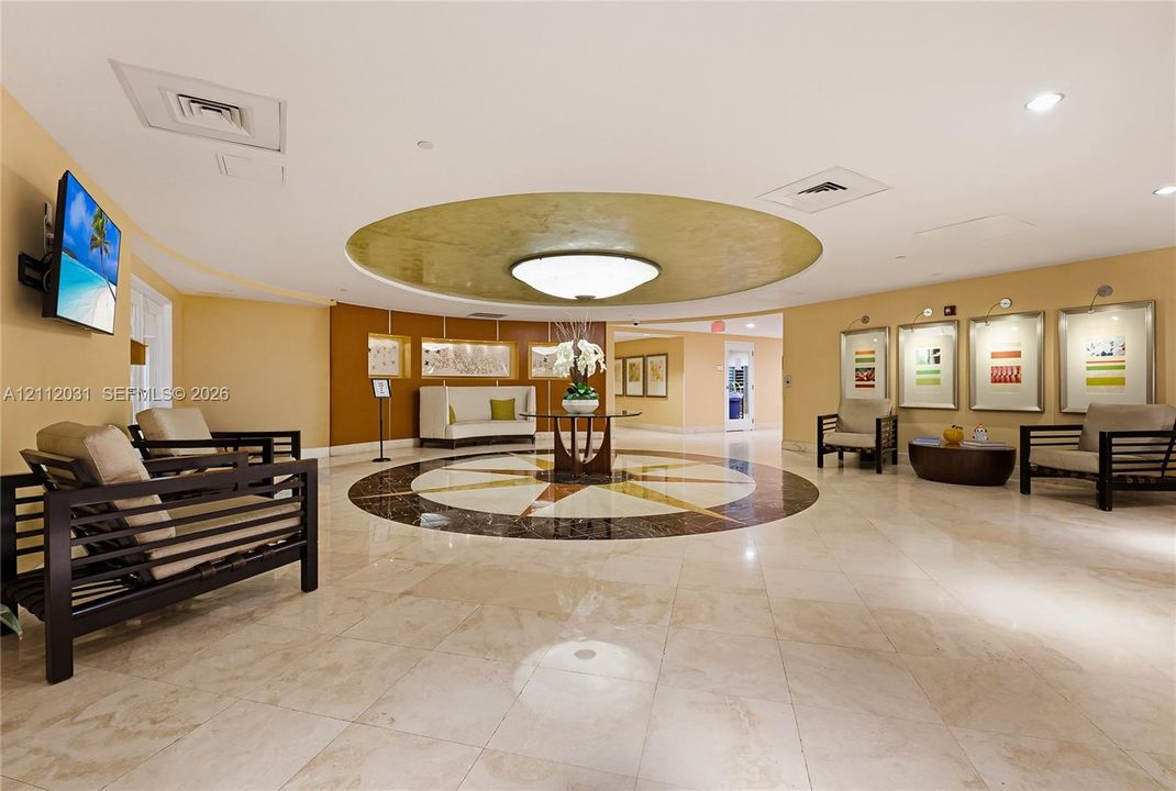 Lobby featuring polished stone tile flooring, circular stone inlay detail, recessed ceiling with gold-toned soffit, and built-in recessed display niches