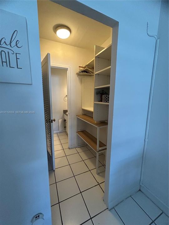 Walk-in closet featuring white built-in shelving, wood-finish shelving tiers, and ceramic tile flooring