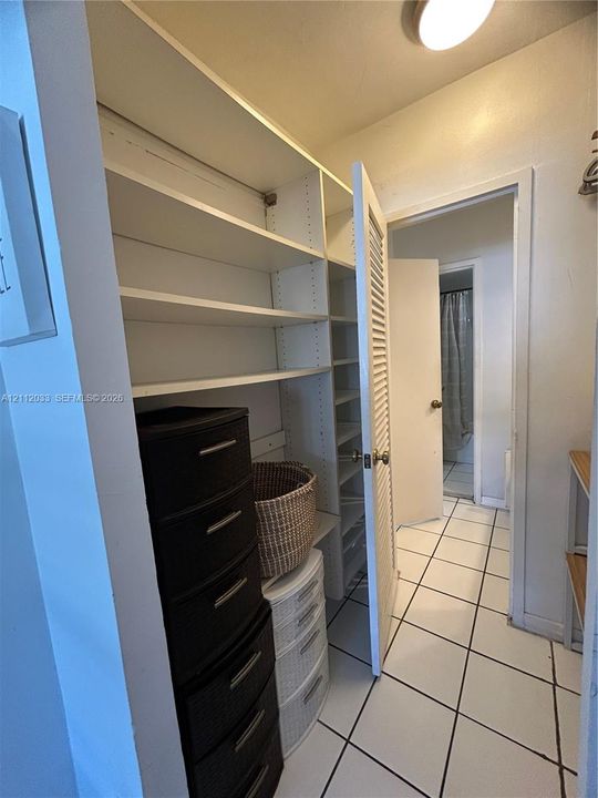 Storage area featuring white adjustable built-in shelving, white louvered closet door, and white floor tiling