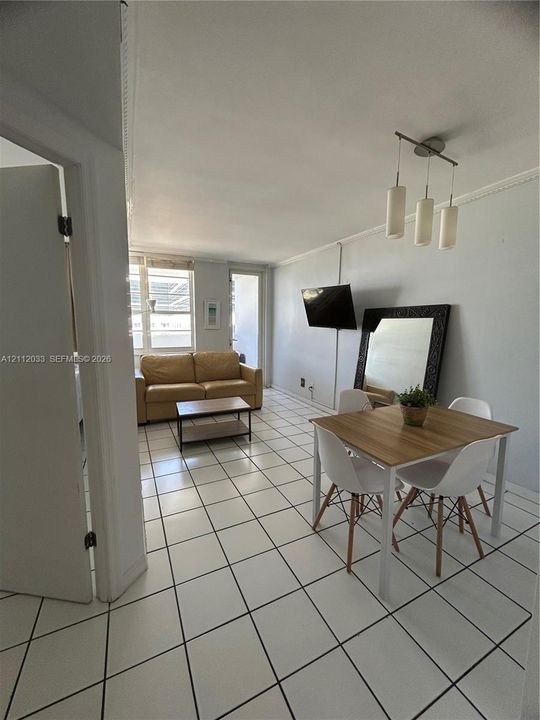 Living area featuring white ceramic tile flooring, a multi-light brushed-metal pendant fixture, and a glass-paneled door