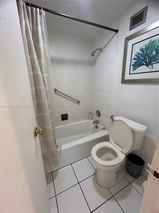 Full bathroom featuring a tub-shower combination with white tiled walls, square-format floor tiling, and a wall-mounted grab bar