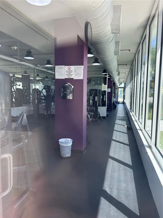 Fitness center featuring floor-to-ceiling windows, exposed industrial ductwork, rubberized flooring, and mirrored walls