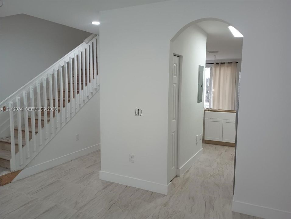Interior featuring light-toned tile flooring, a staircase with white balusters, an arched entryway, and built-in cabinetry
