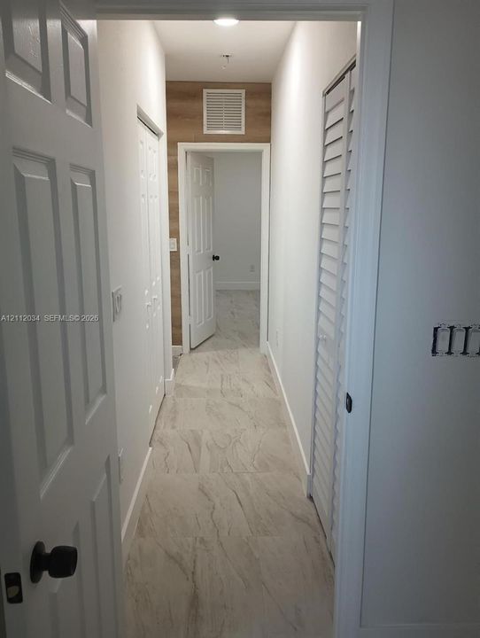 Interior hallway featuring large-format tile flooring, wood-finish wall paneling, and dual louvered closet doors with matte black hardware