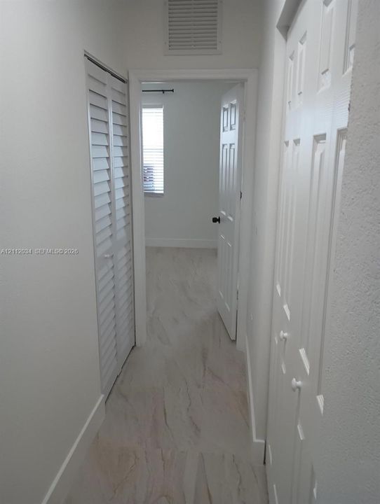 Hallway featuring light-toned tile flooring, louvered closet doors, and six-panel interior doors with matte black hardware