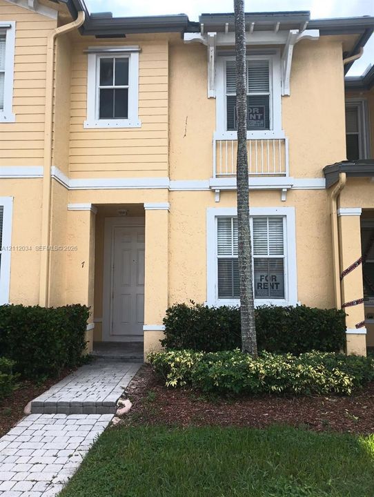 Exterior facade featuring a combination of horizontal lap siding and stucco, a decorative upper-level balcony with railings, white window trim, and a paved brick walkway