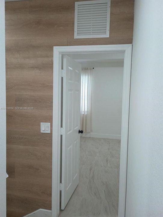Wall featuring wood-finish paneling, white six-panel door, and neutral-toned floor tile