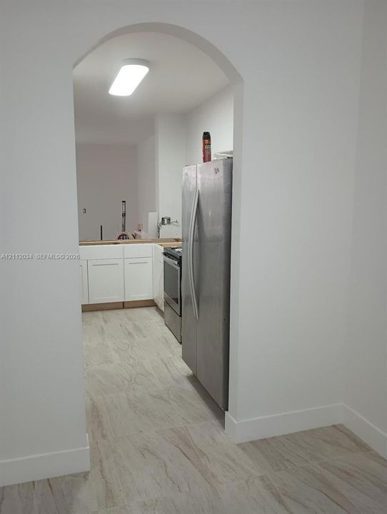 Arched entryway featuring white shaker-style cabinetry, stainless steel refrigerator, stainless steel range, and wood-finish tile flooring