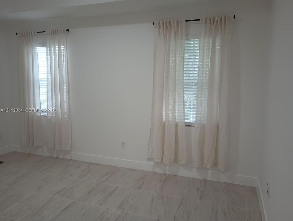 Neutral-toned room featuring stone-finish tile flooring, dual windows, and wall-mounted curtain rods