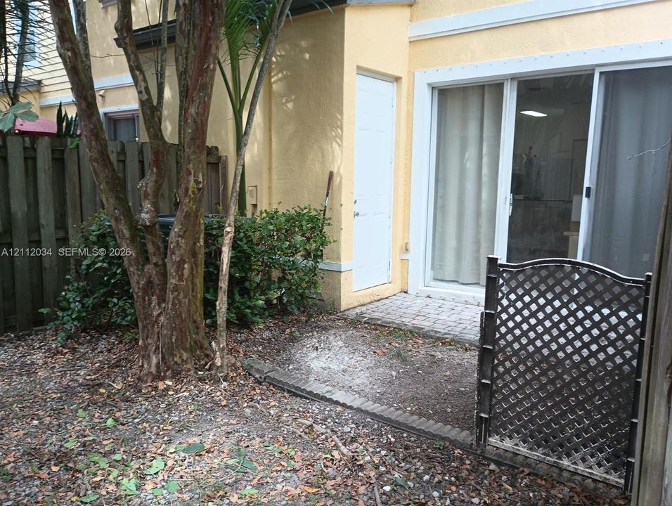 Outdoor patio with paver flooring, sliding glass door, white exterior door, and decorative lattice gate enclosure