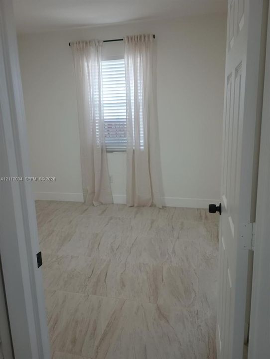 Neutral-toned stone-finish tile flooring, white interior walls, and horizontal blind window covering with matte black door hardware