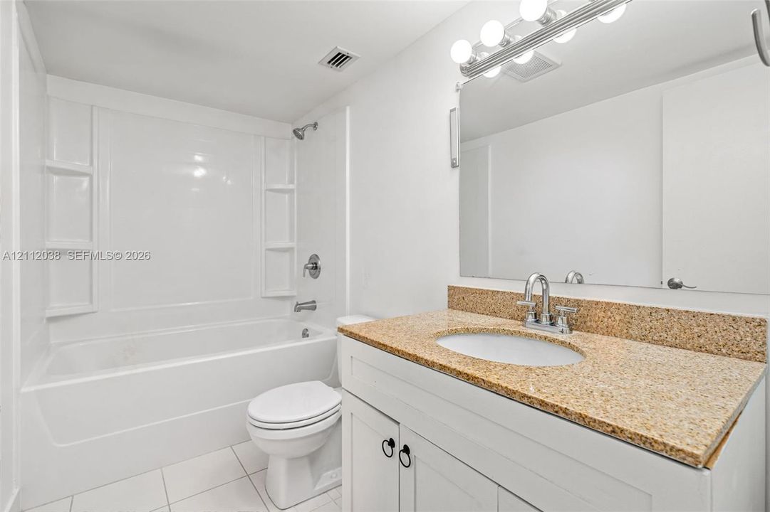 Bathroom featuring a vanity with a stone-finish countertop, undermount sink, multi-bulb lighting, and a bathtub with an integrated surround