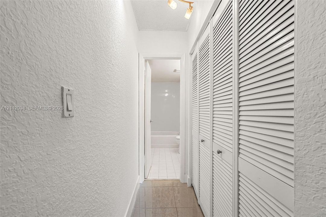 Hallway featuring built-in floor-to-ceiling louvered-style closet doors, neutral wall finish, and tile flooring