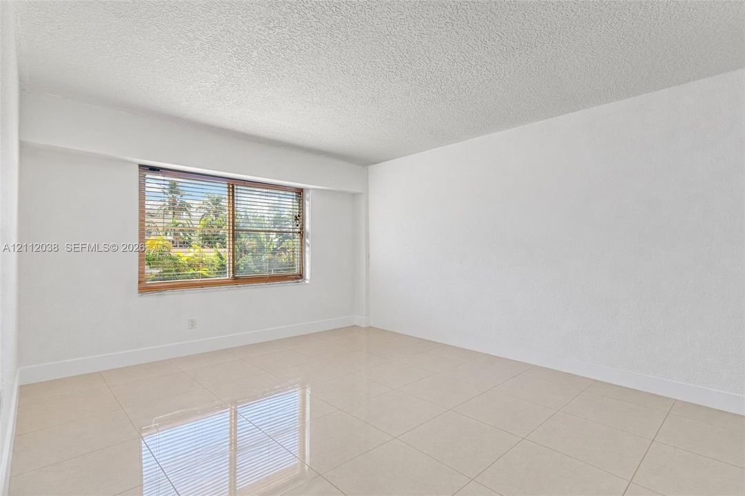 Interior space featuring light-colored tile flooring, smooth wall finishes, a window with integrated blinds, and textured ceiling finish