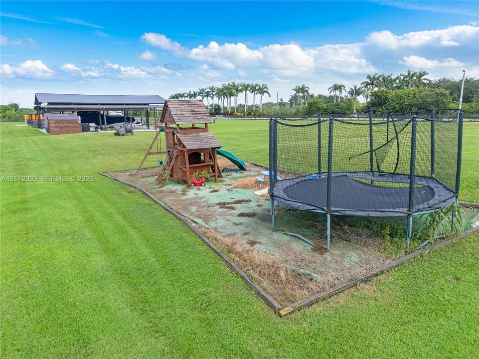 Expansive lawn featuring a detached metal-roofed structure and perimeter fencing