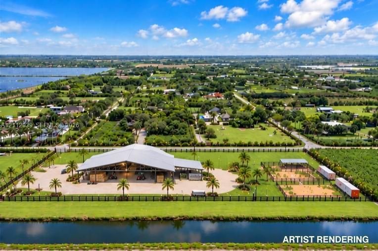 Expansive property featuring a large open-air covered pavilion, multiple fenced enclosures, paved surfaces, mature palm trees, and waterfront canal frontage