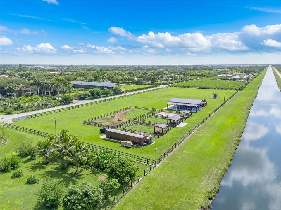 Expansive acreage featuring multi-sectioned fenced paddocks, covered stalls, a central open-air structure, and a canal-front perimeter