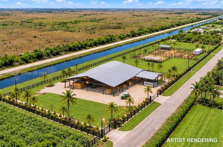 Expansive property featuring an open-air metal structure, perimeter fencing, landscaped grounds with mature palm trees, and canal frontage