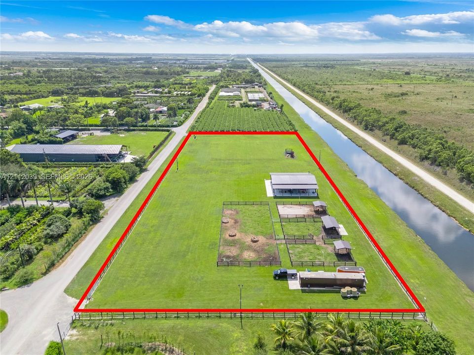 Expansive lot featuring fenced pasture, multiple horse stalls, a covered metal structure, and canal frontage