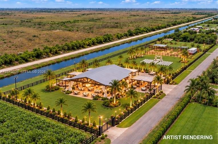 Aerial view of a sprawling property featuring a large open-air pavilion with timber-frame construction and a metal roof, expansive manicured grounds with mature palm landscaping, a perimeter fence, and direct canal frontage
